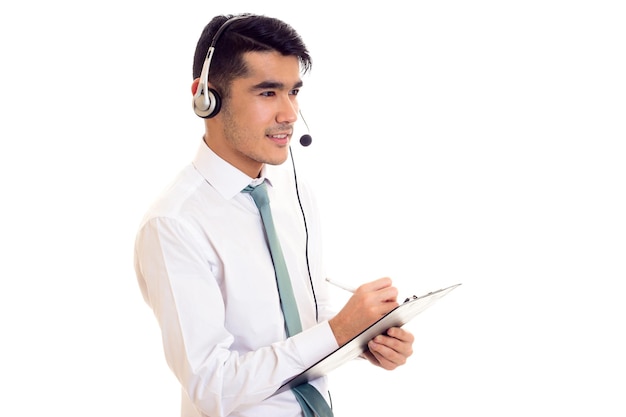 Bom homem com cabelo preto na camisa branca com gravata azul e fones de ouvido segurando uma pasta no fundo branco no estúdio