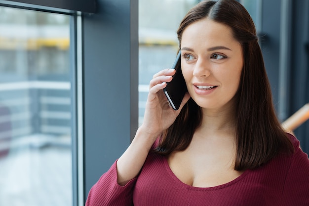 Bom humor. Perto de uma jovem encantadora, olhando pela janela enquanto fala no celular