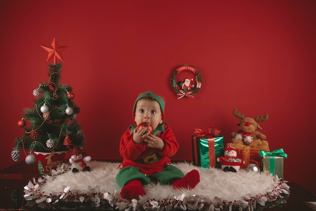Bom rapaz vestido como um elfo ao lado de decorações de Natal com uma árvore e presentes