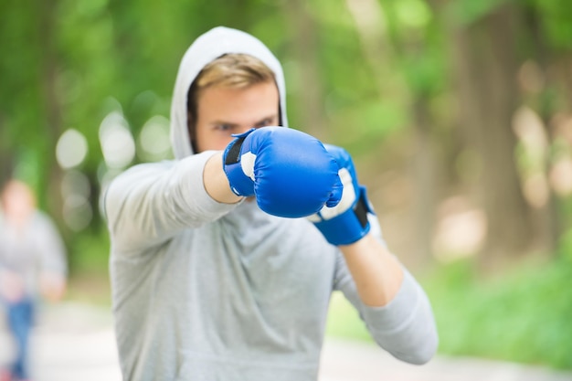 Bom soco Resistência de treinamento de boxe Homem atleta rosto concentrado com luvas esportivas praticando boxe fundo da natureza Boxeador pronto para lutar Treinamento de boxeador esportista com luvas de boxe