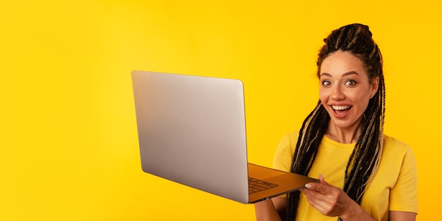 Bom trabalho de laptop. Mulher mostrando sinal legal segurando o computador na sala amarela.