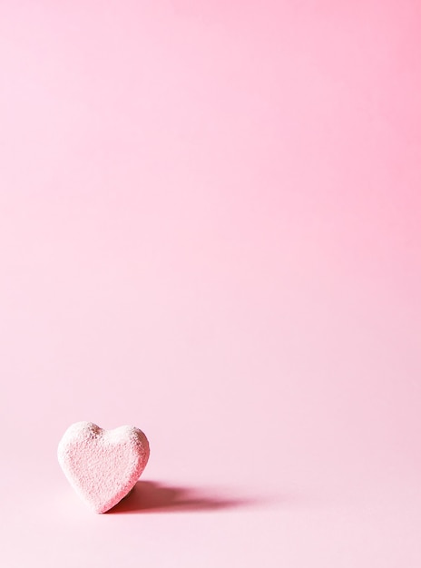 Bomba de baño pequeña rosa en forma de corazón sobre fondo pastel suave.