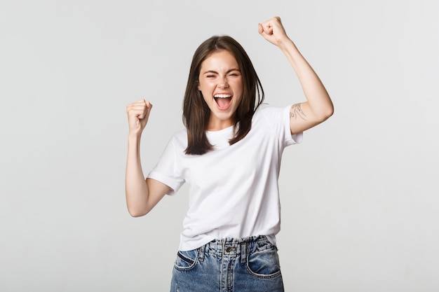 Bomba de puño de chica morena atractiva alegre y sonriendo con regocijo, juego ganador.