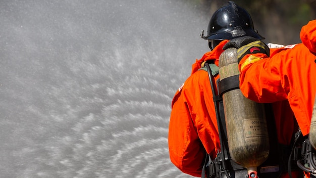 Foto bombeiro asiático em serviço de combate a incêndios bombeiro asiático pulverizando água de alta pressão bombeiro em equipamento de combate a incêndio uniforme pulverizar água da mangueira para combate a incêndios
