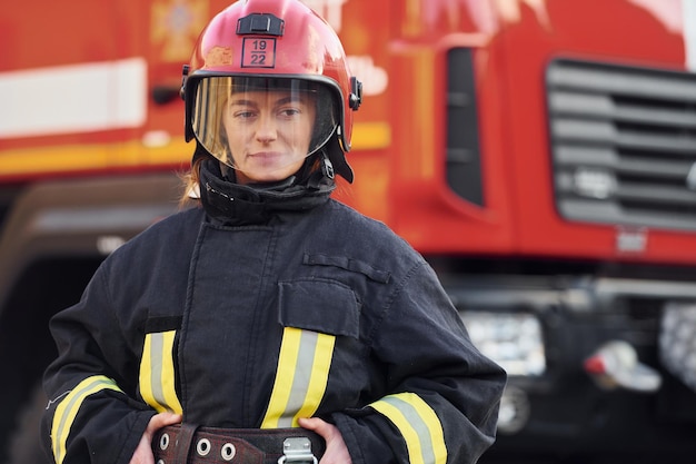 Bombeiro feminino em uniforme de proteção em pé perto de caminhão