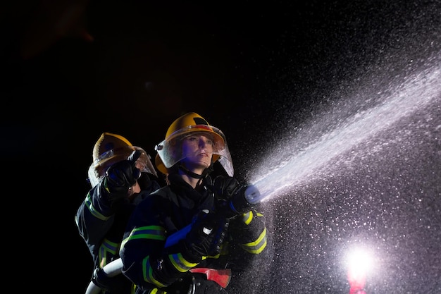 Bombeiros usando uma mangueira de água para eliminar um risco de incêndio. Equipe de bombeiros femininos e masculinos em perigosa missão de resgate. foto de alta qualidade