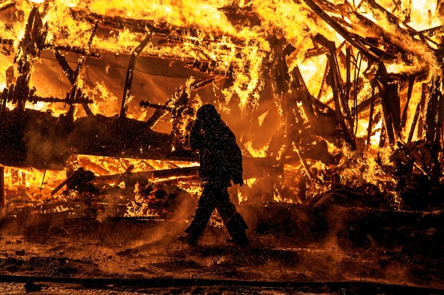 Foto bombero caminando junto a un fuego ardiente por la noche