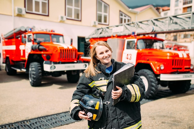 Bombero femenino en un traje protector con documentos de pie en el fondo de un camión de bomberos