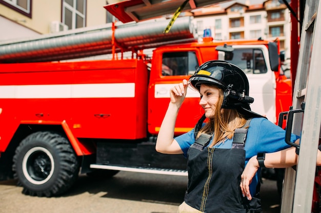 Bombero femenino en uniforme protector de pie cerca de camión de bomberos rojo