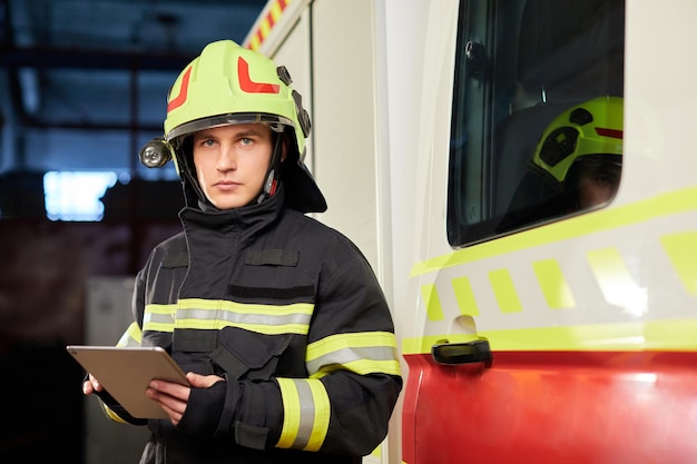 Bombero masculino con tableta en uniforme en el fondo del coche