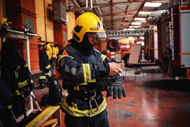 Bombero poniéndose el uniforme protector y preparándose para la acción mientras está de pie en la estación de bomberos.