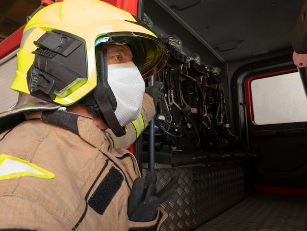 Bombero subiendo al camión equipado con casco y máscara de traje de intervención para protegerse del covid 19