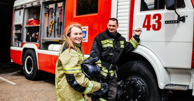 Bomberos mujer y hombre en cascos cerca de camión de bomberos Rescate de protección del peligro Estación de bomberos