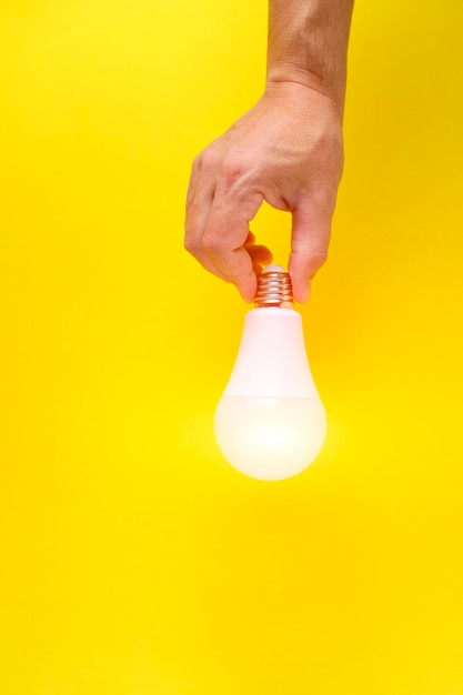 Bombilla LED ecológica en la mano sobre fondo amarillo