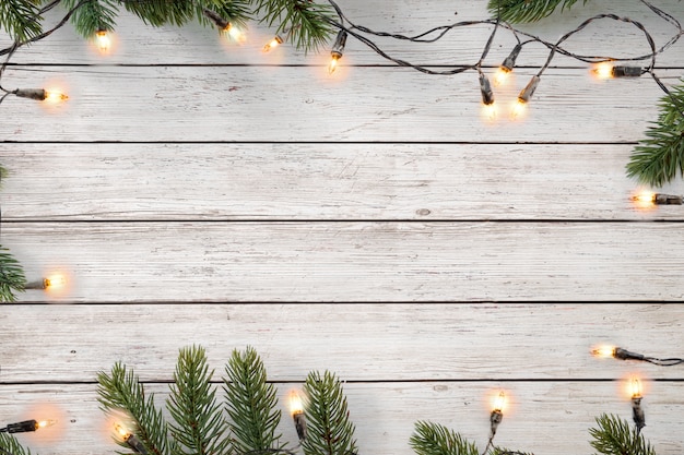 Bombilla de luces de Navidad y decoración de hojas de pino en tablón de madera blanca, diseño de borde de marco. Fondo de vacaciones feliz Navidad y año nuevo. vista superior.