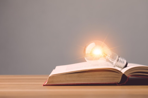 Bombilla de luz clara con efecto de luz en el libro antiguo y puesta en un escritorio de madera con fondo de pared de espacio gris Idea de aprendizaje Concepto de educación