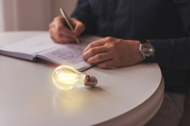 Bombilla de luz encendida se encuentra sobre una mesa cerca de una innovación de idea de hombre de negocios de escritura