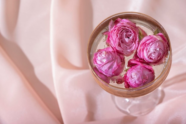 Bombillas de vista superior en champán alrededor de rosas en el vaso sobre fondo textil doblado Bodegón hermoso creativo