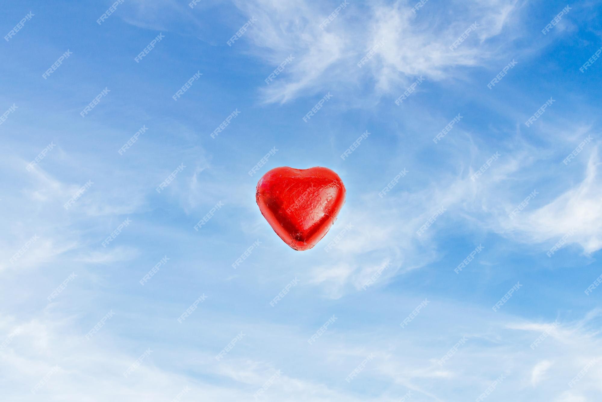 Bombón de chocolate en forma de corazón envuelto en lámina roja sobre un  fondo azul con nubes blancas. | Foto Premium