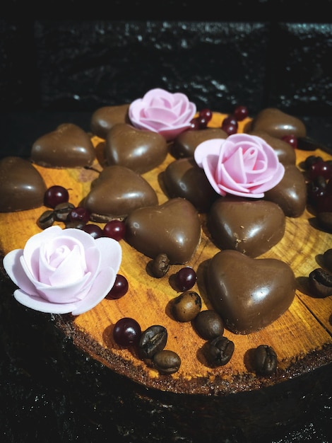 Bombons de chocolate apetitosos em um fundo escuro em um corte de madeira com flores e grãos de café