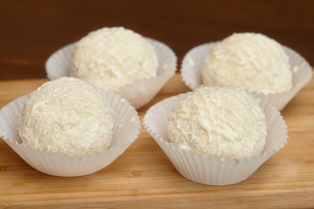 Bombons de chocolate branco com cobertura de coco na superfície de madeira