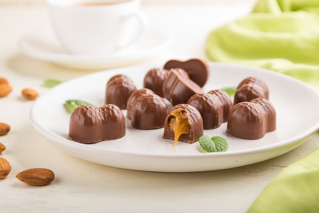 Bombons de chocolate com amêndoas e caramelo em uma madeira branca.