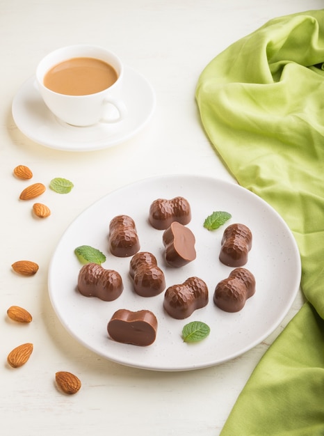 Bombons de chocolate com amêndoas e uma xícara de café em uma madeira branca.