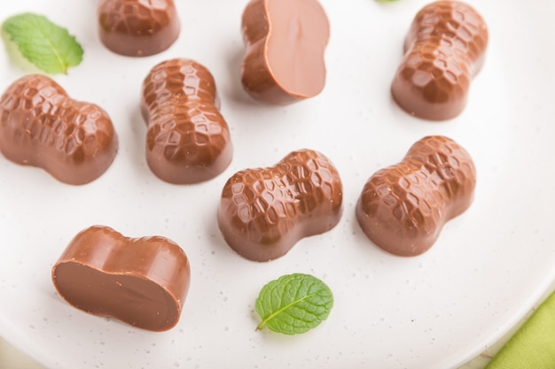 Bombons de chocolate com amêndoas em uma superfície de madeira branca e tecido verde