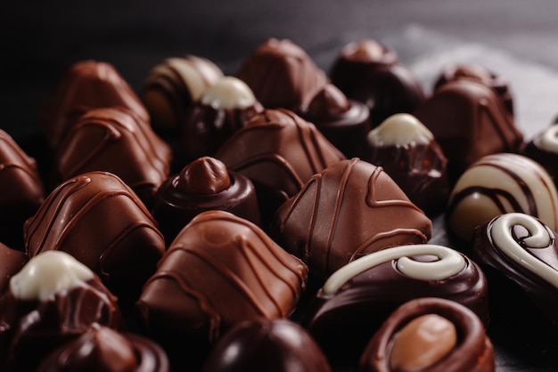 Bombons de chocolate com diferentes alimentos doces saborosos doces de chocolate em um fundo escuro para