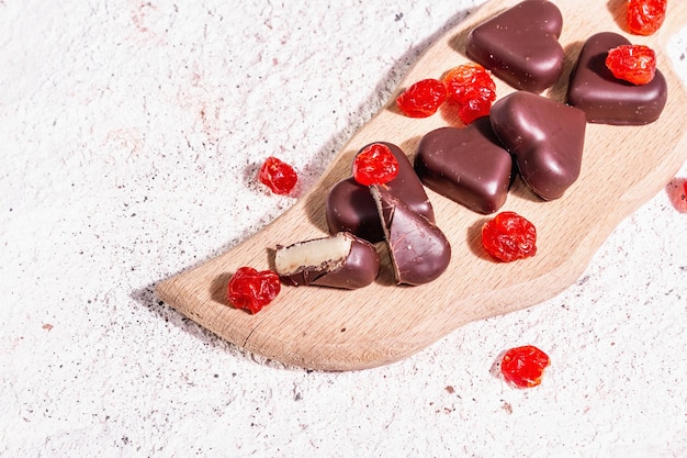 Bombons de chocolate em forma de coração com cerejas secas. Luz dura moderna, sombra escura. Um presente doce para o dia dos namorados ou aniversário. Fundo de gesso em tons claros, vista de cima