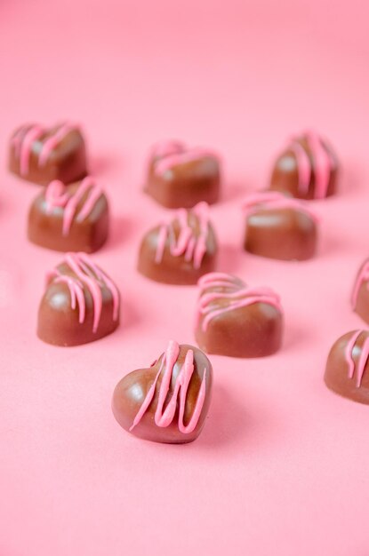 Bombons de chocolate em forma de coração com glacê rosa Fundo liso rosa