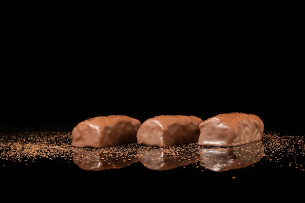 Bombons de chocolate em uma superfície escura com reflexo. Recheio de nozes e frutas. Copie o espaço.