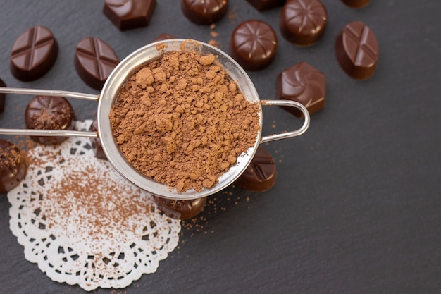 Foto bombons de chocolate em uma superfície preta, cacau em pó. foto escura, humor.