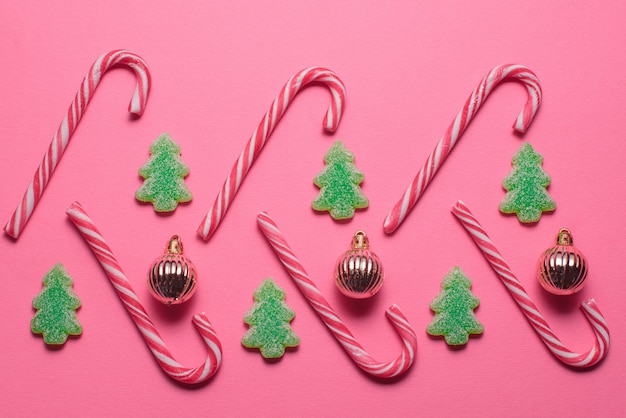Bonbons in Form eines Weihnachtsbaumes und goldener Kugeln liegen auf rosafarbenem Hintergrund, Draufsicht. Weihnachts- und Neujahrskonzept
