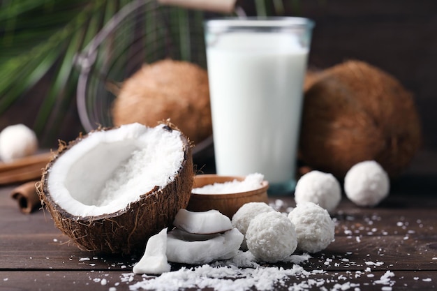 Bonbons in Kokosflocken, Glas Milch und frischer Kokosnuss auf dunklem Holzhintergrund