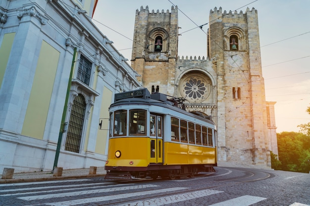 Foto bonde amarelo típico subindo no bairro de alfama em frente à catedral de lisboa - portugal