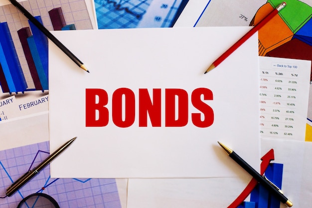 Bonds é escrito em uma superfície branca perto de gráficos coloridos, canetas e lápis. conceito de negócios