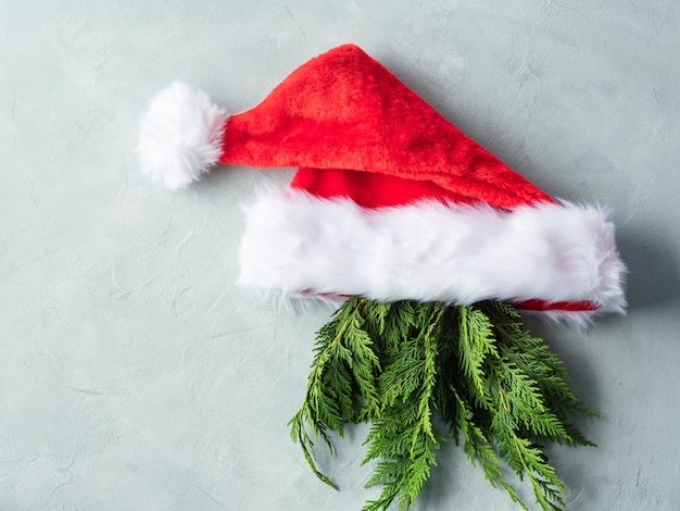 Boné de Papai Noel com galhos de árvores de abeto como barba no conceito mínimo de natal de fundo cinza