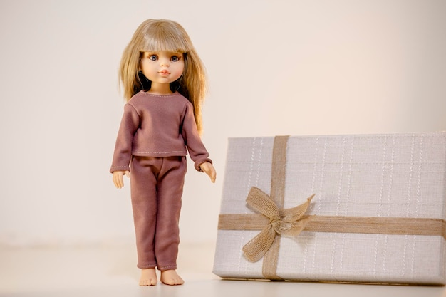 Boneca bonita demonstrando seu pijama e de pé ao lado do presente Sessão de fotos de boneca fofa