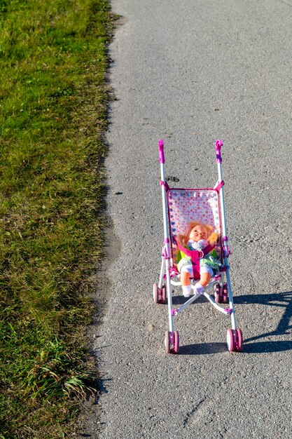 Foto boneca de brinquedo macio em uma carruagem de brinquedo parada na estrada, vista de um conceito perigoso de carrinho de bebê