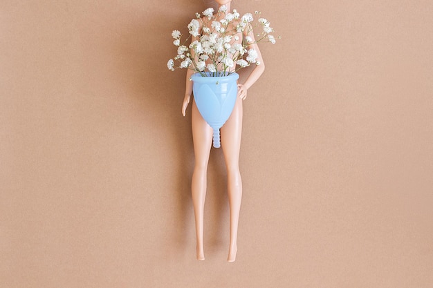 Boneca de mulher segura copo menstrual azul com flores delicadas de buquê em fundo marrom com espaço de cópia Higiene íntima feminina Conceito de saúde de mulheres ecologicamente corretas alternativas de desperdício zero
