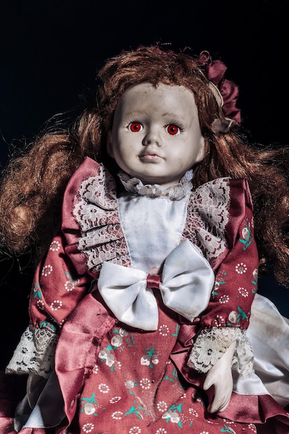 Boneca de porcelana suja velha com olhos vermelhos assustadores em um fundo escuro conceito de Halloween