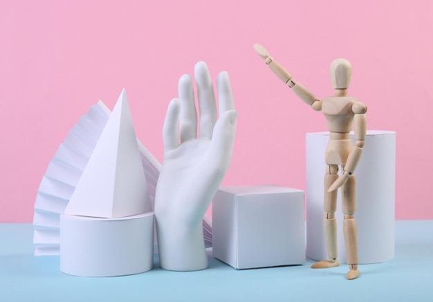 Foto boneco de madeira de figuras geométricas e mão em um fundo pastel bluepink composição de diferentes objetos geométricos arte conceitual minimalismo de fundo abstrato