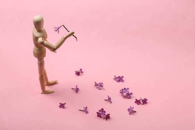 Boneco de madeira segurando flores em um fundo rosa Conceito de amor romântico