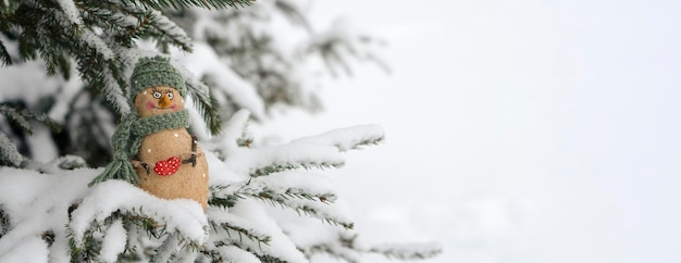 Foto boneco de neve, brinquedo no fundo de uma árvore de natal com neve. nevando. foco seletivo, fundo desfocado do inverno. o conceito do próximo ano novo.