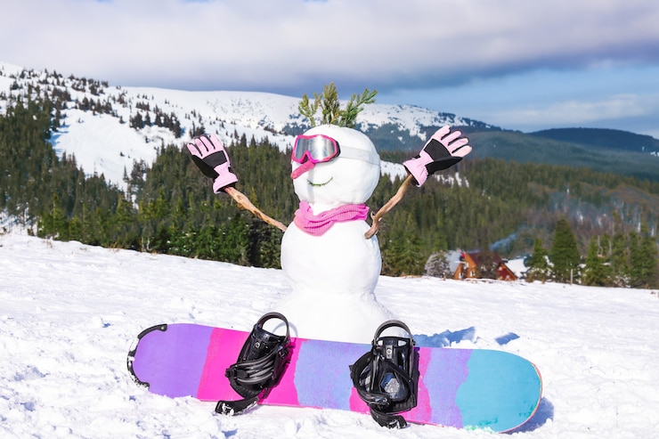 Foto boneco de neve com snowboard na estância de montanha de esqui em dia ensolarado. férias de inverno
