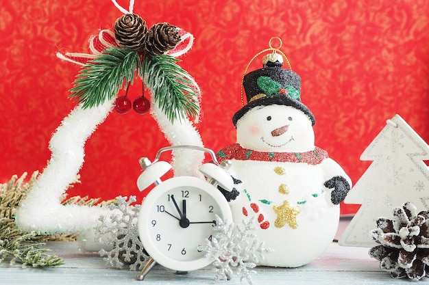 Boneco de neve de brinquedo de natal, despertador, floco de neve de prata e enfeites de natal em um fundo vermelho.