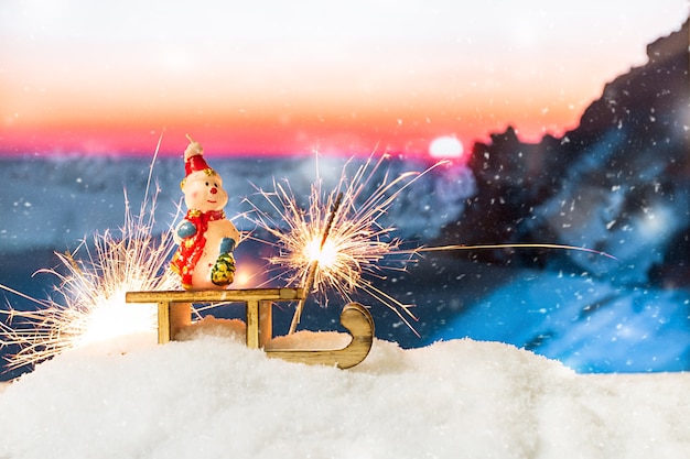 Boneco de neve em um trenó em um monte de neve na frente de montanhas nevadas