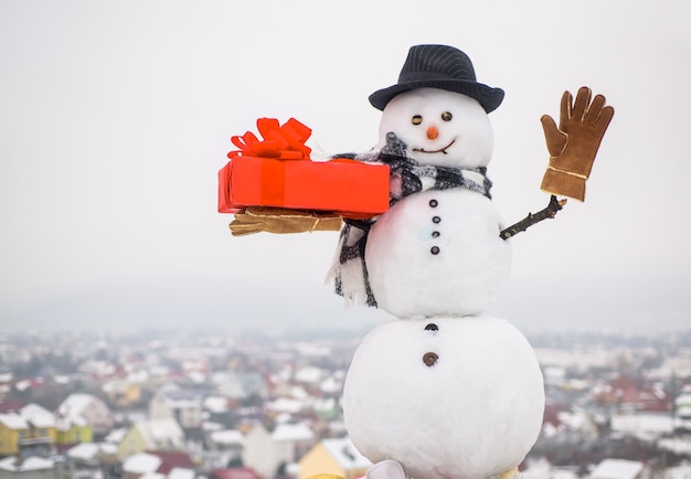 Foto boneco de neve feliz com presente acenando boneco de neve com presente caixa boneco de neve com chapéu lenço luvas de natal