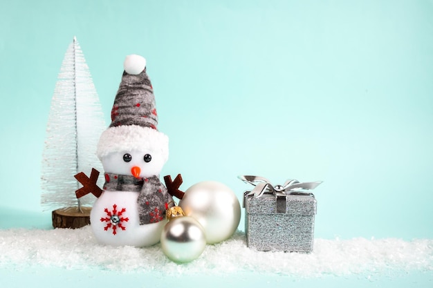 Boneco de neve presente árvore de Natal bola de Natal na neve branca em um fundo turquesa Lugar para uma inscrição